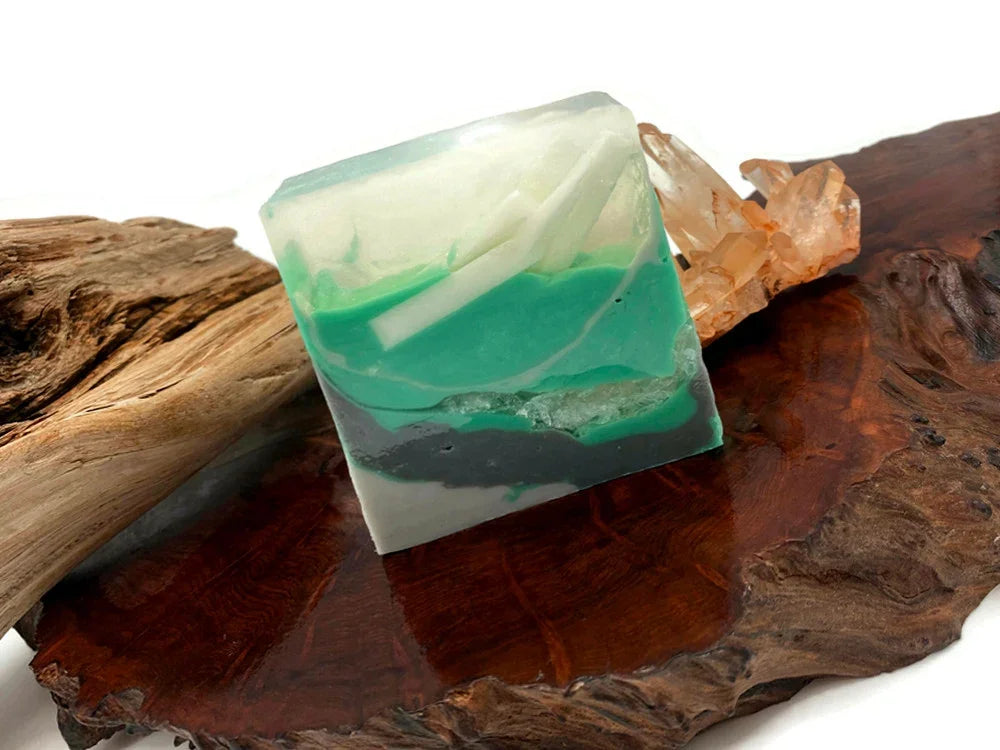Handmade teal and white marbled soap bar on a rustic wood slab with crystals.