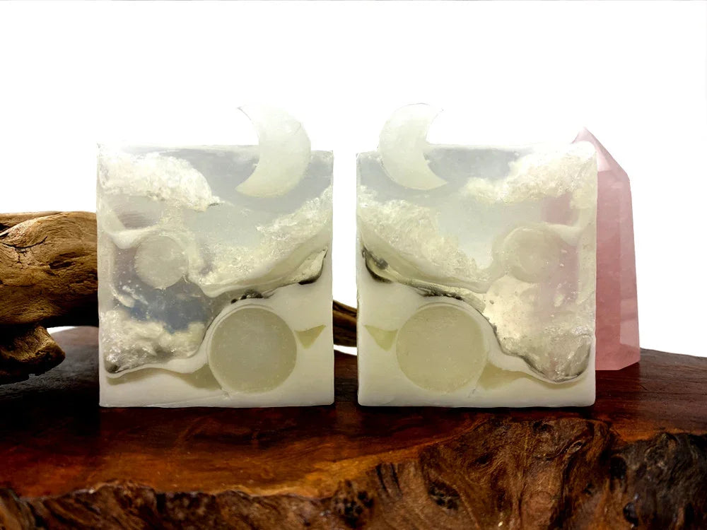 Handmade white soap bars with celestial moon and cloud designs on wood.