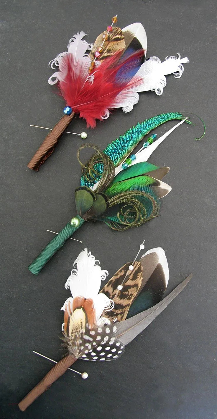 Three handcrafted decorative feather boutonnieres in red, green, and brown tones.