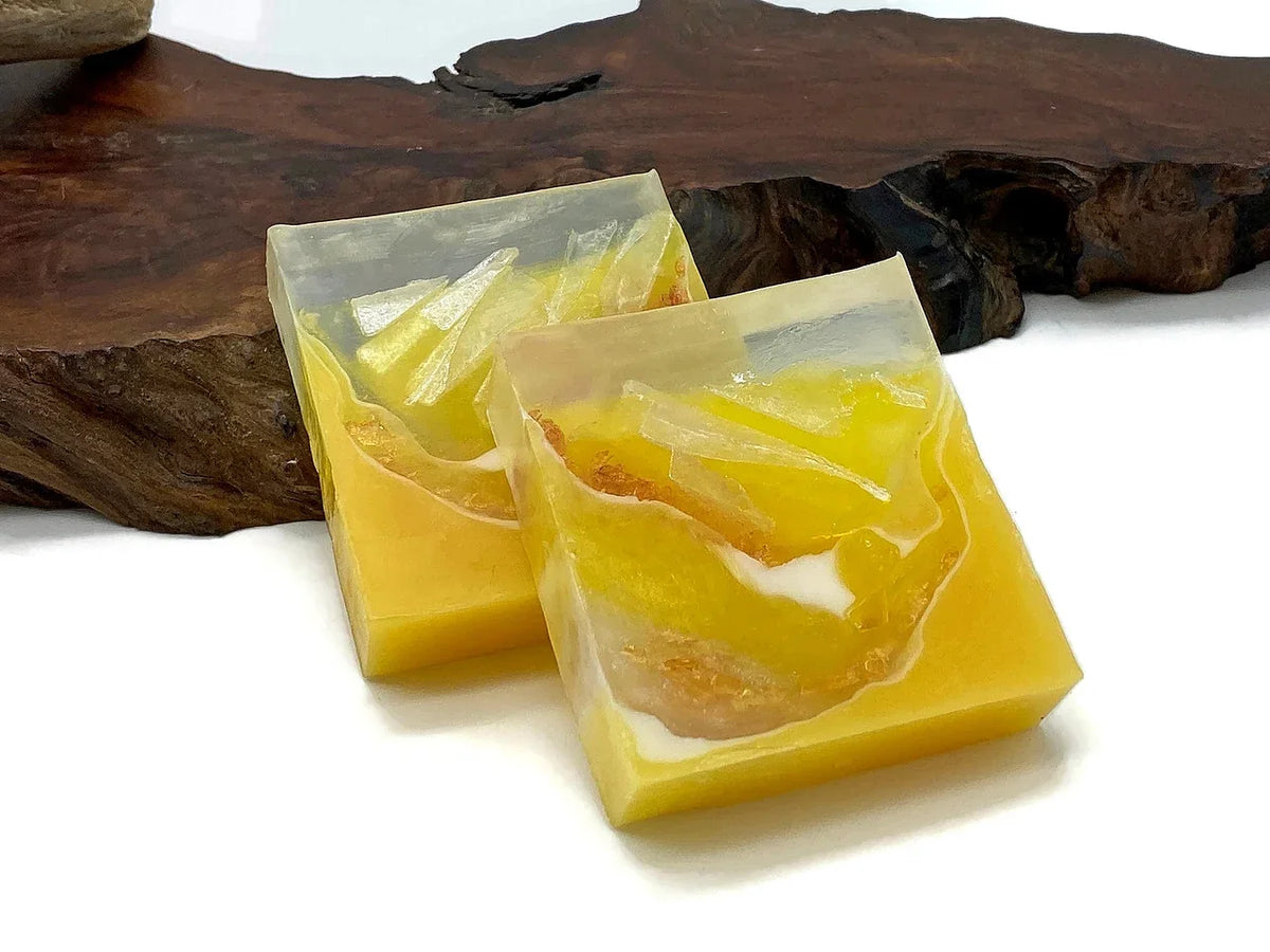 Two square yellow resin coasters with gold leaf accents on a wooden surface.