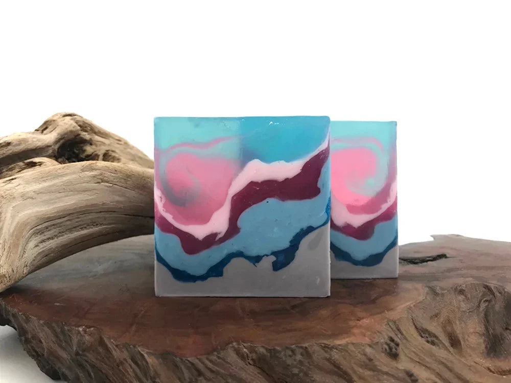 Handmade swirl soap bars with blue, pink, and purple marble patterns on a wood base.