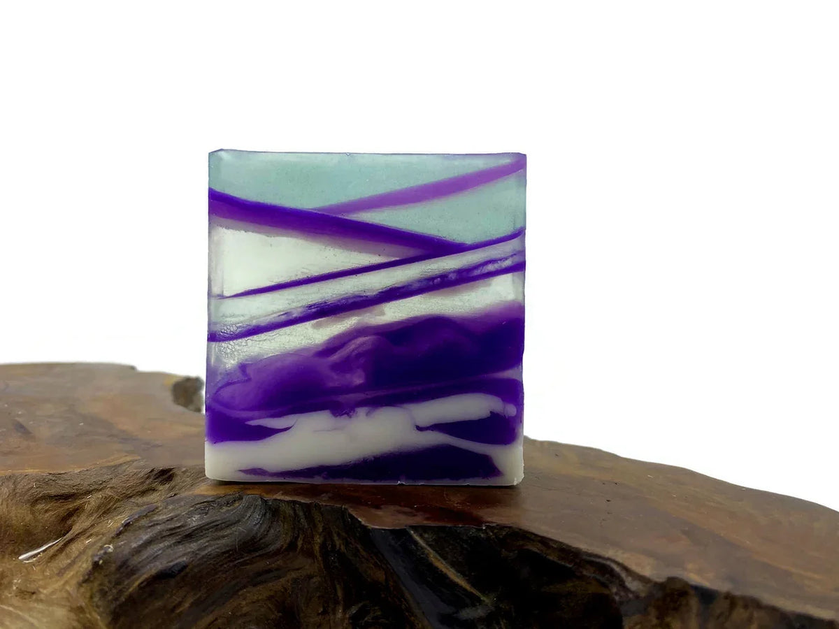 Handmade square soap with purple and white marble swirls on a wooden base.