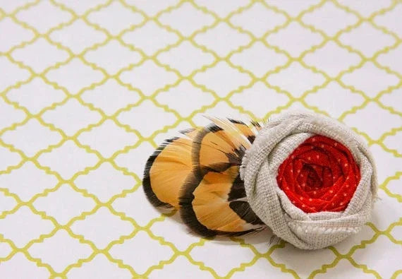 Fabric rose hair accessory with tan and black striped feathers on a patterned background.