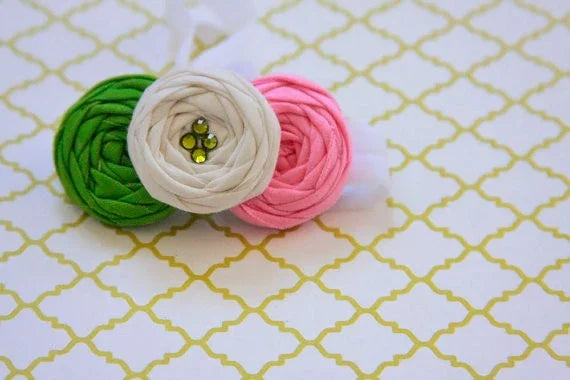 Handmade fabric rosette hair accessories in green, white, and pink with rhinestone center.