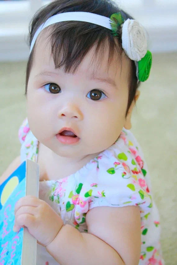 Cute baby girl wearing a floral headband and pink floral print dress holding a blue book.