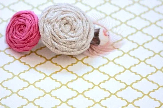 Pink and beige fabric rose hair clip with delicate decorative feathers on gold pattern.
