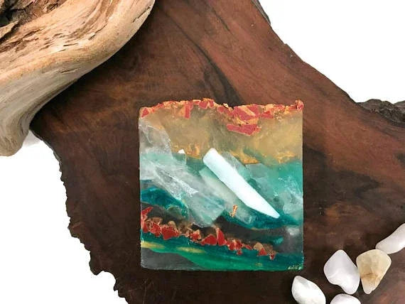 Handmade resin coaster with turquoise, gold, and red mineral inclusions on wood.