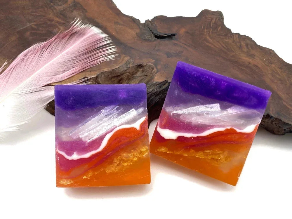 Handmade purple and orange resin square earrings with abstract wave patterns and a pink feather.