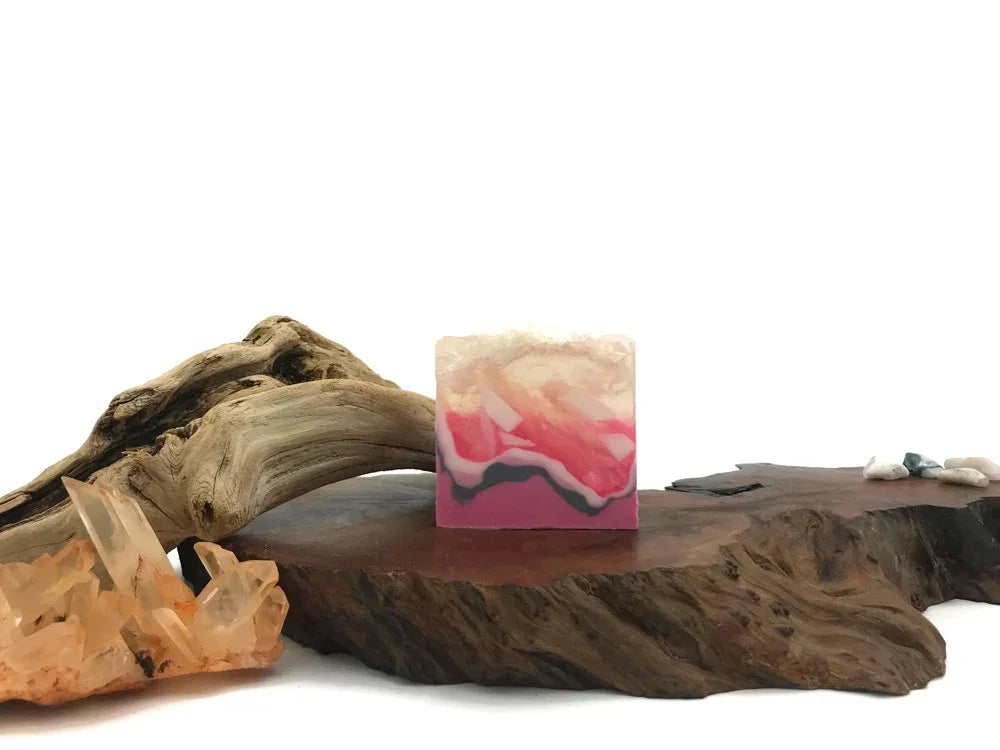 Pink and white marbled handmade soap bar on a rustic wooden base with crystals and driftwood.