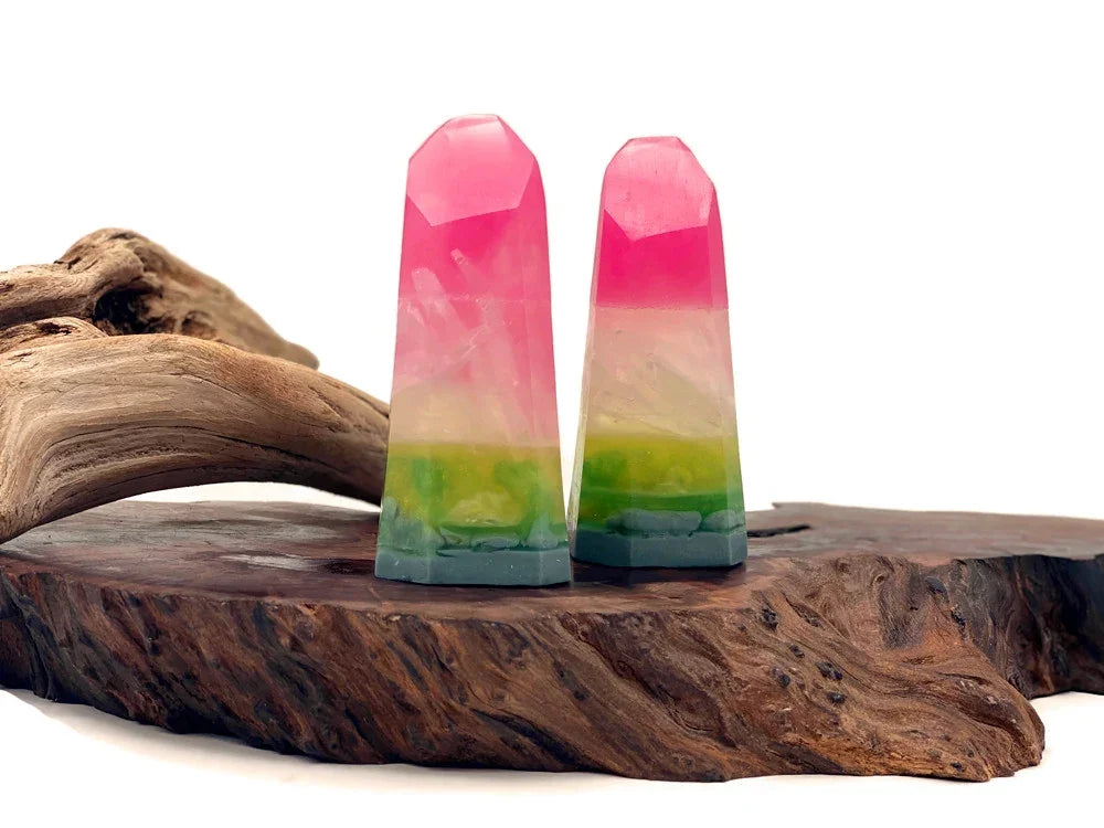 Two pink and green layered resin crystal towers on a natural wood base.