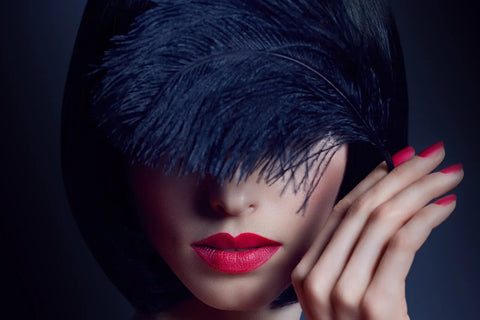 Woman wearing a sweeping black feather headpiece over her eyes.