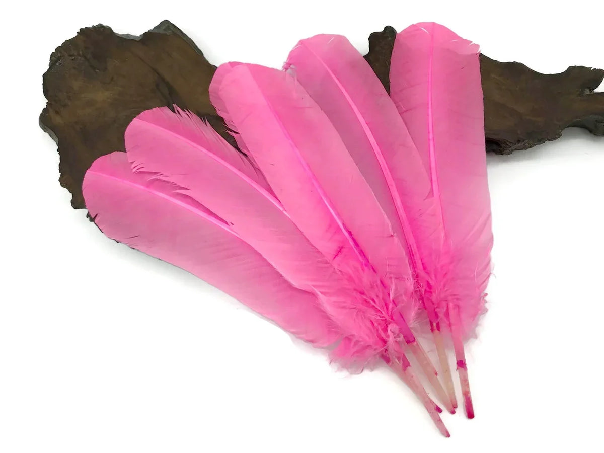Vibrant pink dyed feathers for DIY crafts and fashion decor on a dark wood base.