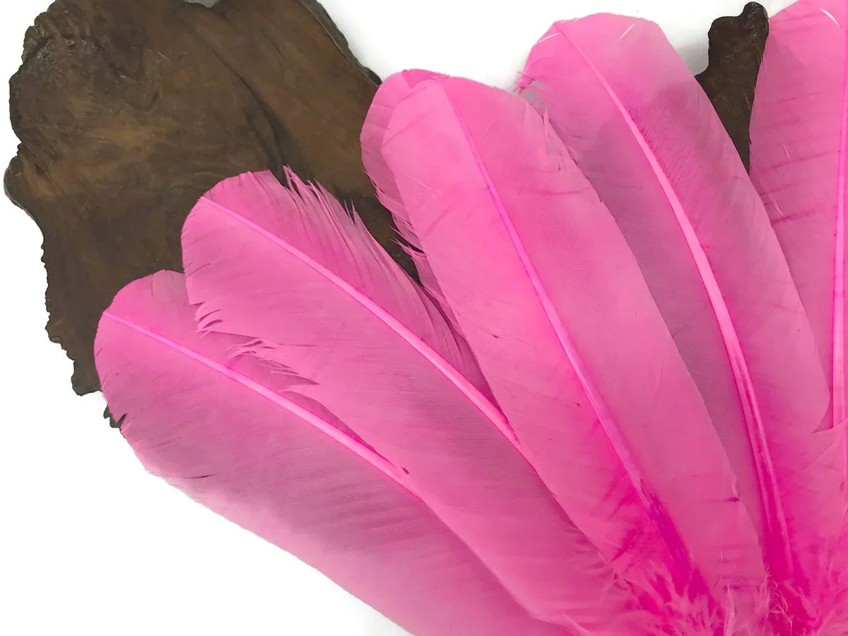 Vibrant pink craft feathers arranged on a dark wooden base for DIY fashion and decor.