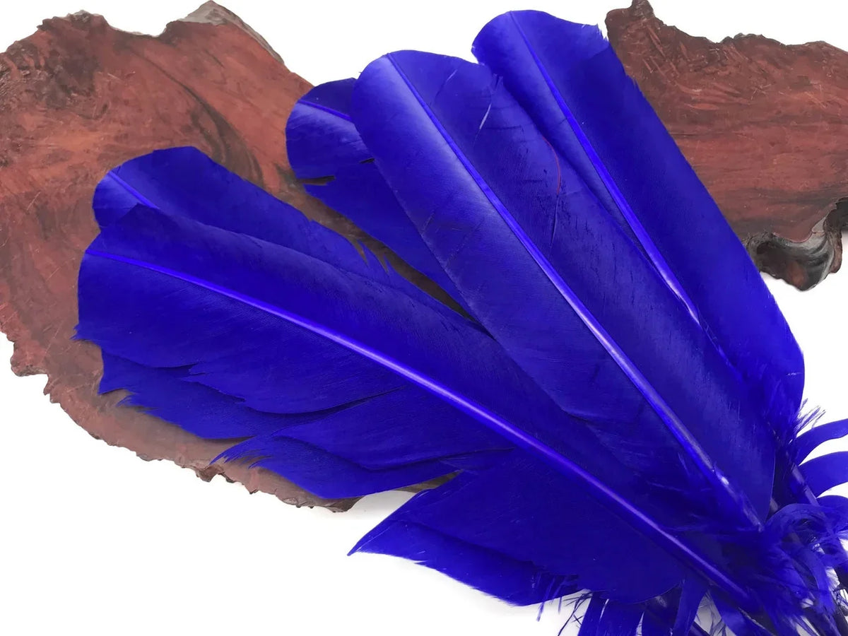 Vibrant cobalt blue feathers for DIY crafts and fashion decor on a rustic wood slice.